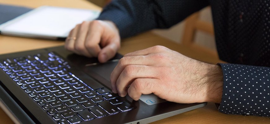 Ett par händer i närbild. De vilar på ett tangentbord på en dator.