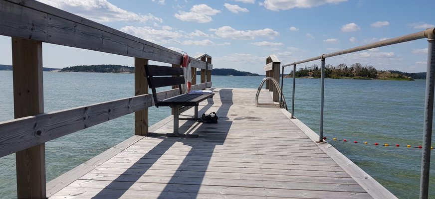 En träbrygga som vätter ut mot ett blått vattendrag.