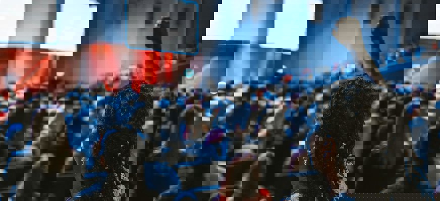 En folksamling i ett mörkt konferensrum. En kvinna med rastaflätor höjer sin knutna näve mot taket.