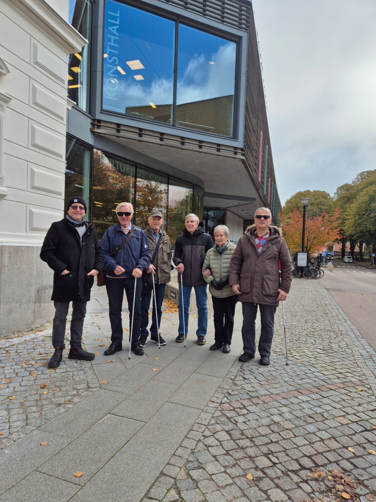 Sex personer, 4 med vit käpp framför Komedianten