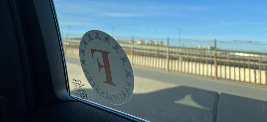 Bild inifrån bil, utanför blå himmel, på rutan färdtjänstlogotyp.