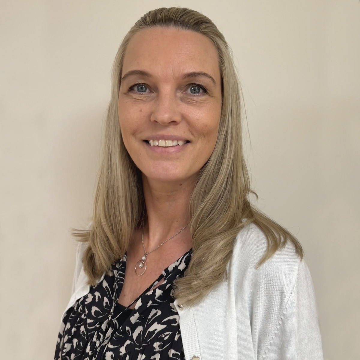 Leende kvinna i 45-årsåldern, långt askblont hår, svartvit blus, vit kofta.