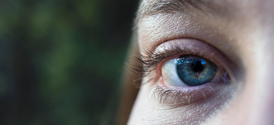Närbild på ett öga taget med grön utomhusmiljö i bakgrunden.