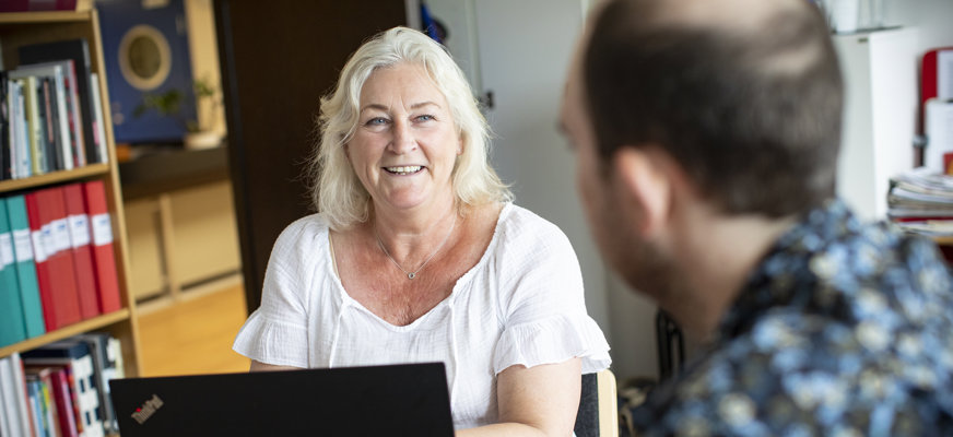 Kvinna vid dator tittar leende mot person mittemot