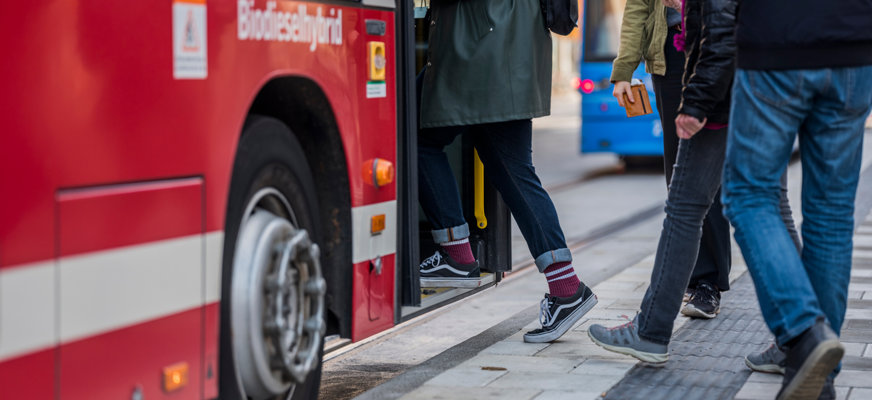 En rad människor som kliver på en röd stadsbuss. 