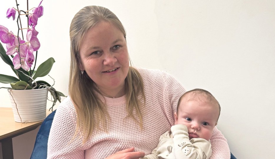 Josefin har rosa tröja och blont hår. Hon håller i en liten bebis med pigg blick och lite brunt hår på huvudet.