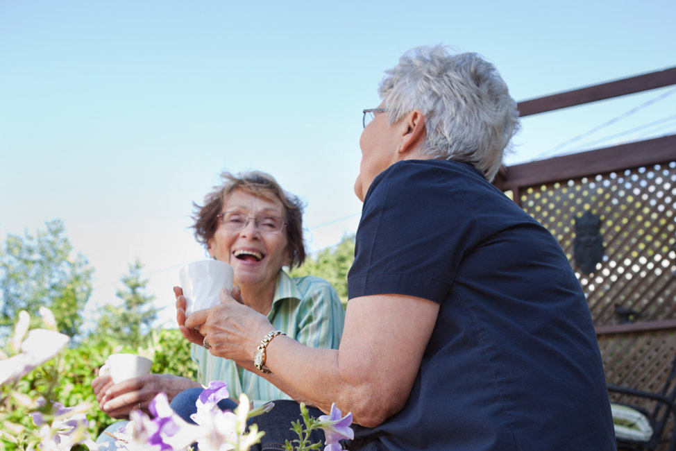 Två äldre kvinnor skrattar på terass