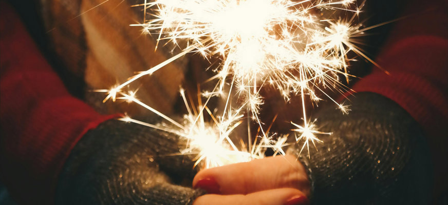 Vantklädda händer som håller i ett sprakande tomtebloss.