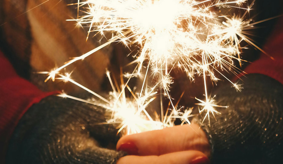 Vantklädda händer som håller i ett sprakande tomtebloss.