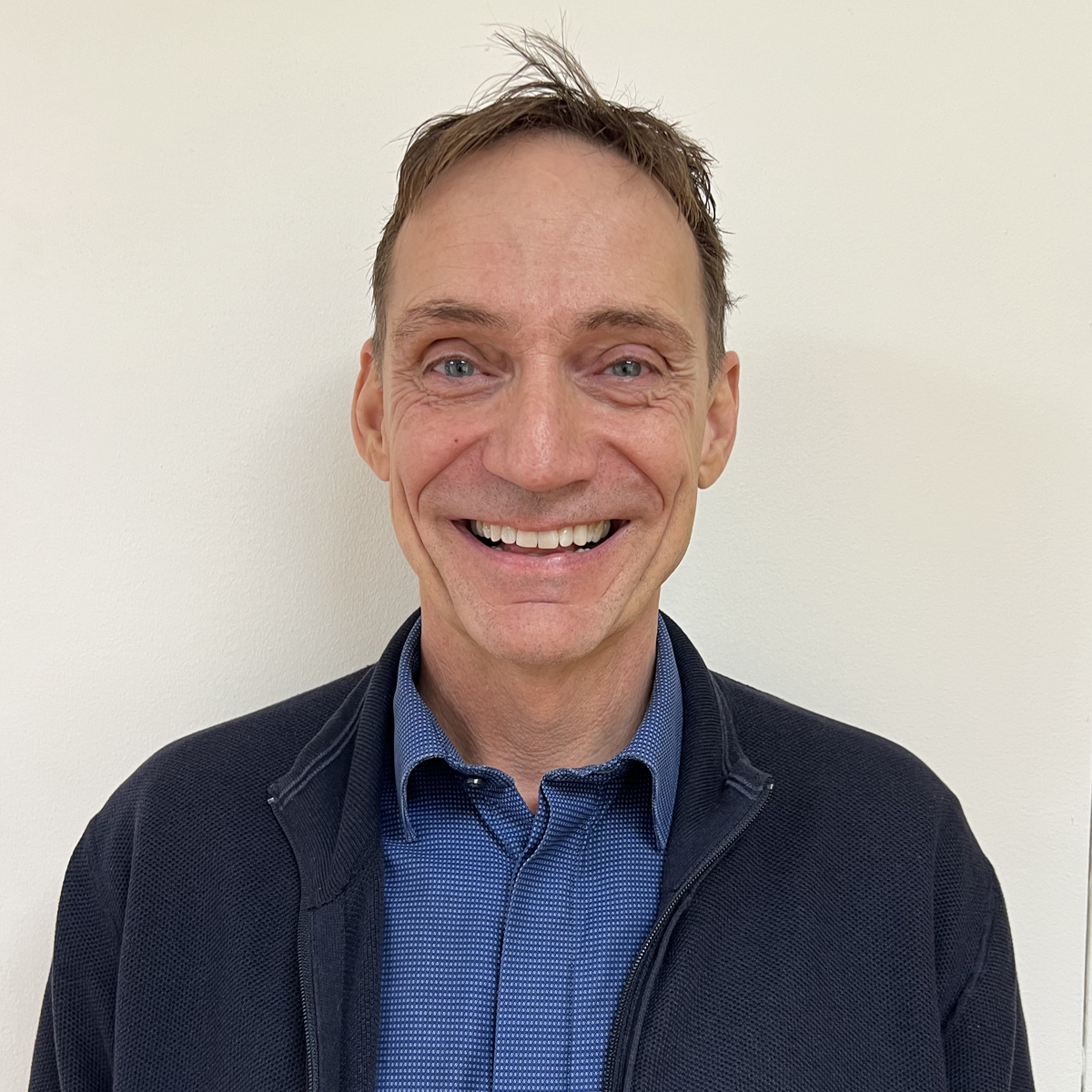 Man i 50-årsåldern, stort leende, kort brunt hår, blå skjorta, mörkblå kofta.
