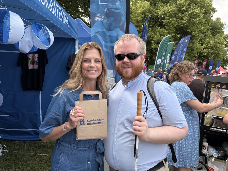 Linus Forsberg tillsammans med Liza-Maria Norlin, partisekreterare (KD). Liza-Maria har mellanblont hår med mittbena som räcker ner över axlarna. Hon bär en blå jeansklänning och poserar leende framför kameran med en papperpåse med SRF-logga.