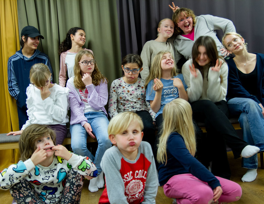 13 barn uppställda för kameran för porträttfoto. Alla tramsar, gör grimaser, skrattar, gör peace-tecken.