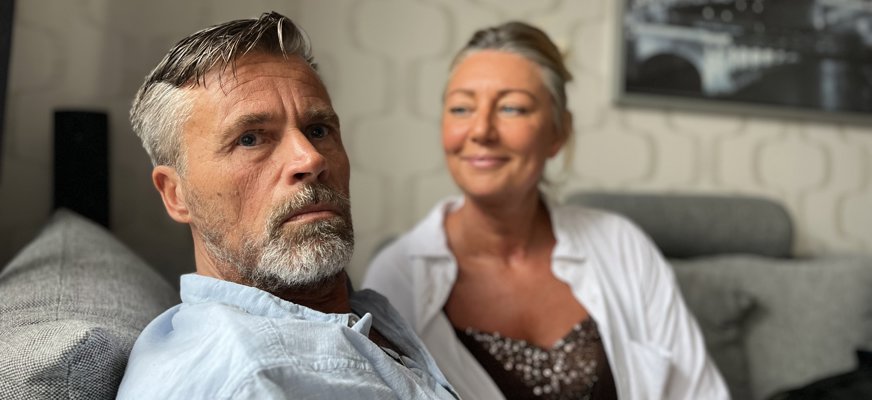 Kenneth och Sofie sitter i en soffa. Kenneth har grått hår och helskägg. Han ser rakt in i kameran. Sofie sitter bredvid och tittar på honom med kärleksfull blick. Hon har uppsatt hår och solkysst hy.