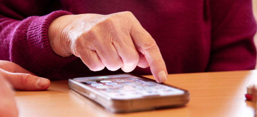 En person som trycker på en iPhone-skärm. I bild är bara handen och telefonen, som ligger på ett bord, synliga.