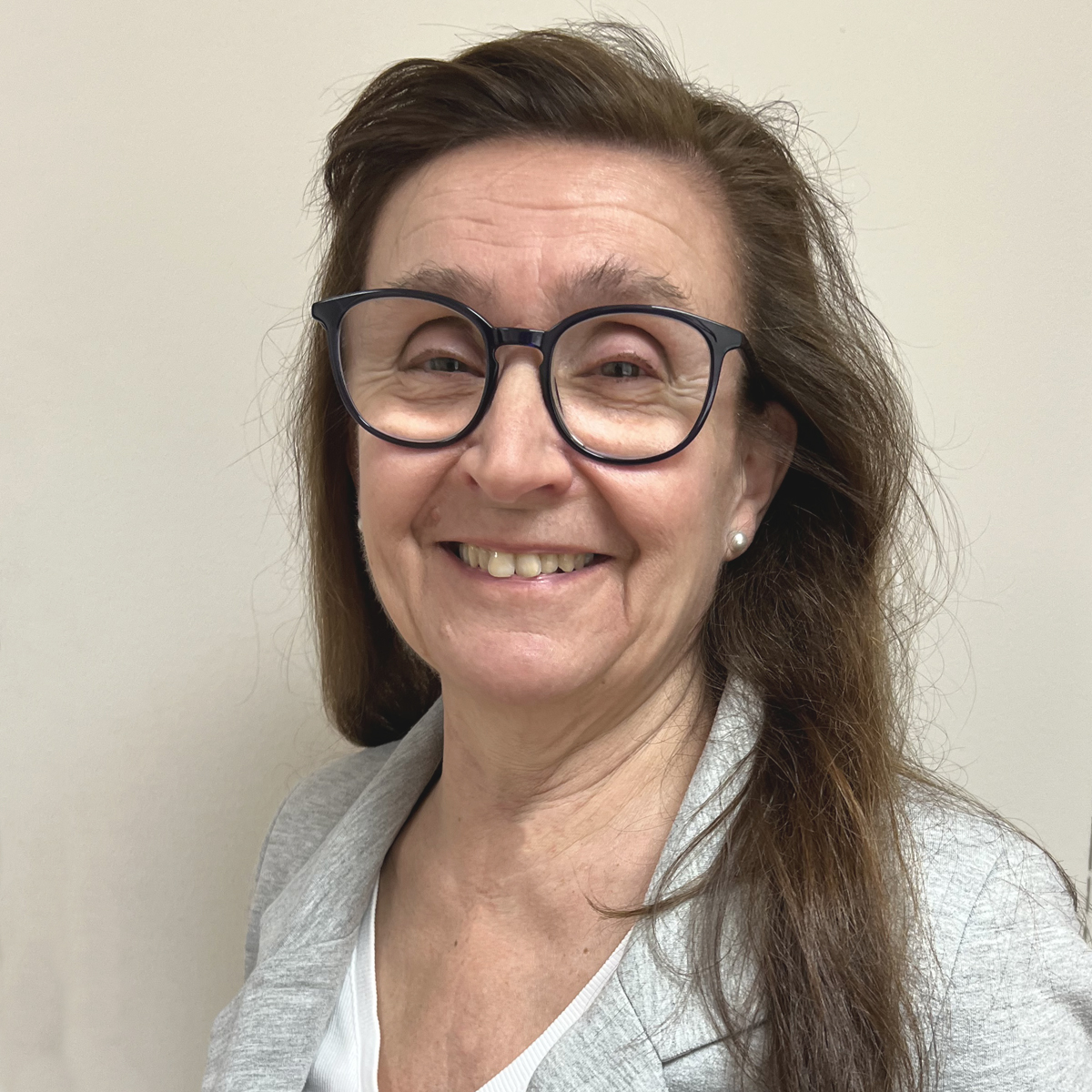 Leende kvinna i 60-årsåldern med långt brunt hår, glasögon och grå kavaj.