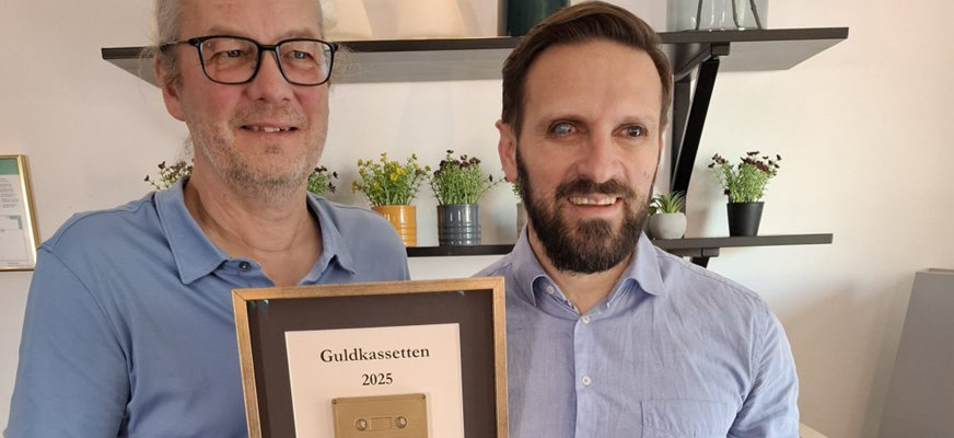 Johan Lunner tillsammans med Fatmir Seremeti. Johan håller i sin inramade guldkassett och båda ler mot kameran.