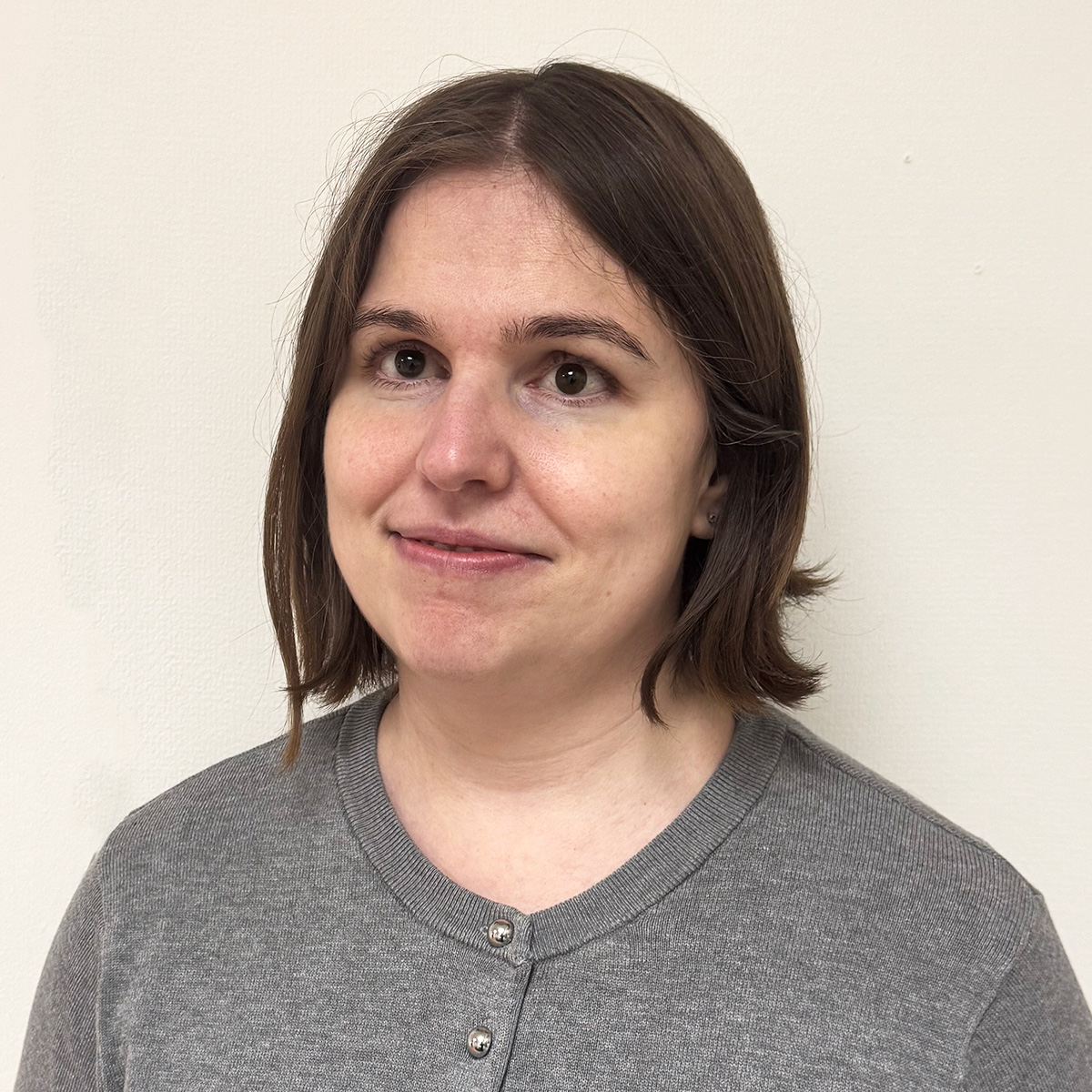 Kvinna i 40 års-åldern med bruna ögon och brunt hår klippt i page med mittbena. Hon har en grå kofta på sig och ler mot kameran.