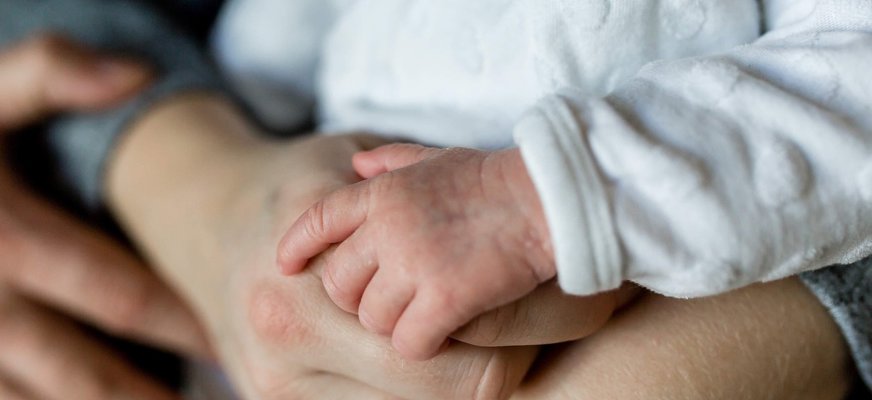 Närbild på en bebishand som håller om pekfingret på en vuxen hand.