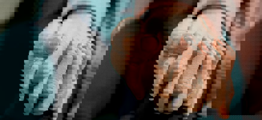 Två händer som håller i varandra, vilandes mot ett knä.