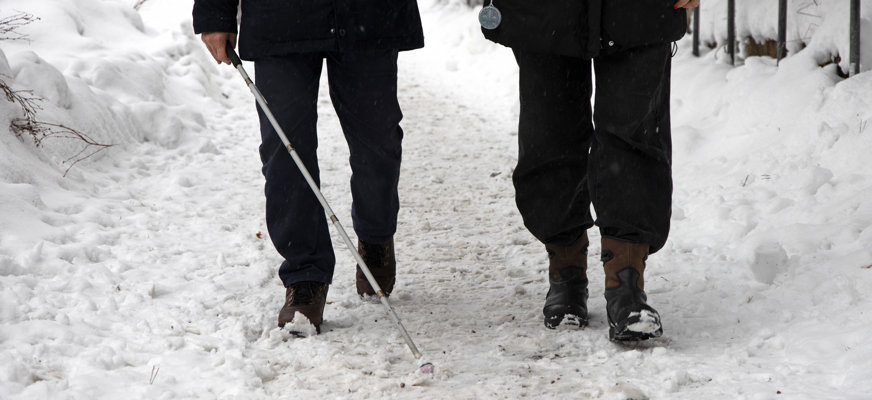 En person med vit käpp blir ledsagad i snöigt landskap.