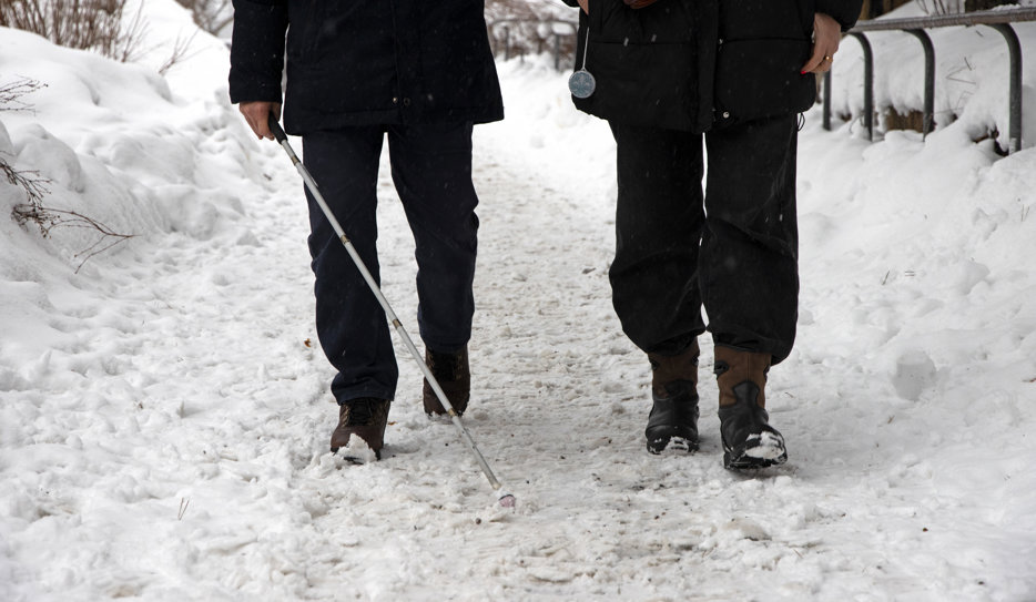 En person med vit käpp blir ledsagad i snöigt landskap.