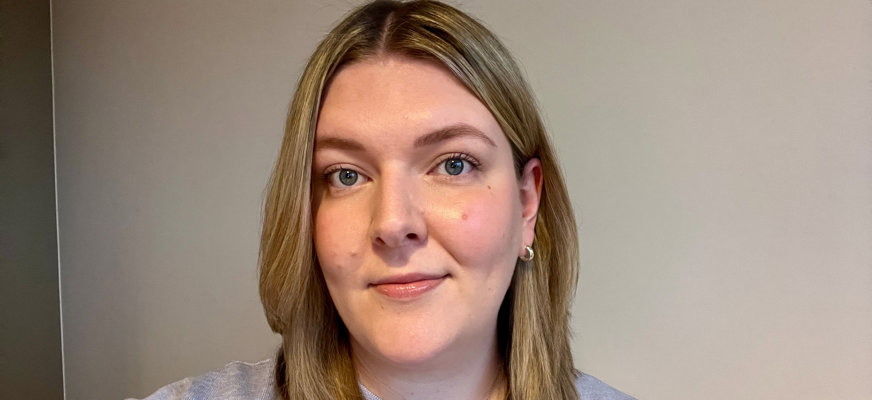 Ebba tittar in i kameran. Hon har mörkblont hår som sträcker sig till nyckelbenen och en ljuslila tröja.