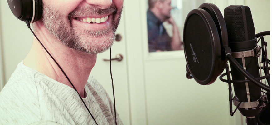 En leende man med hörlurar står framför en studiomikrofon.