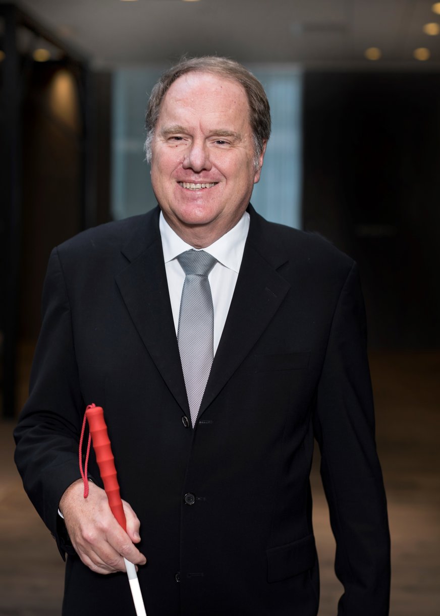 Per Karlström leendes i kostym, vit käpp.
