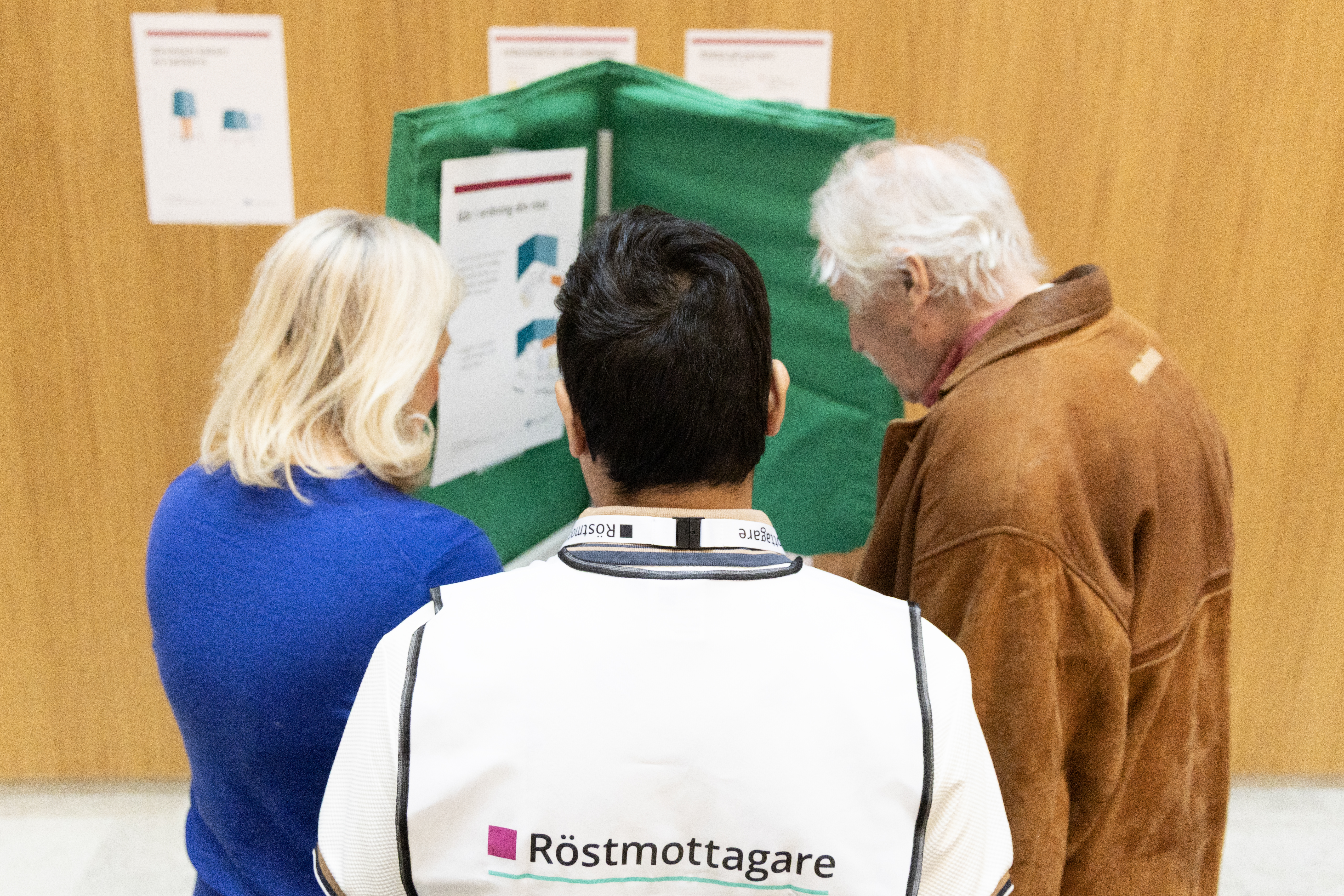 Äldre man i röstningsbås. Två personer assisterar honom.